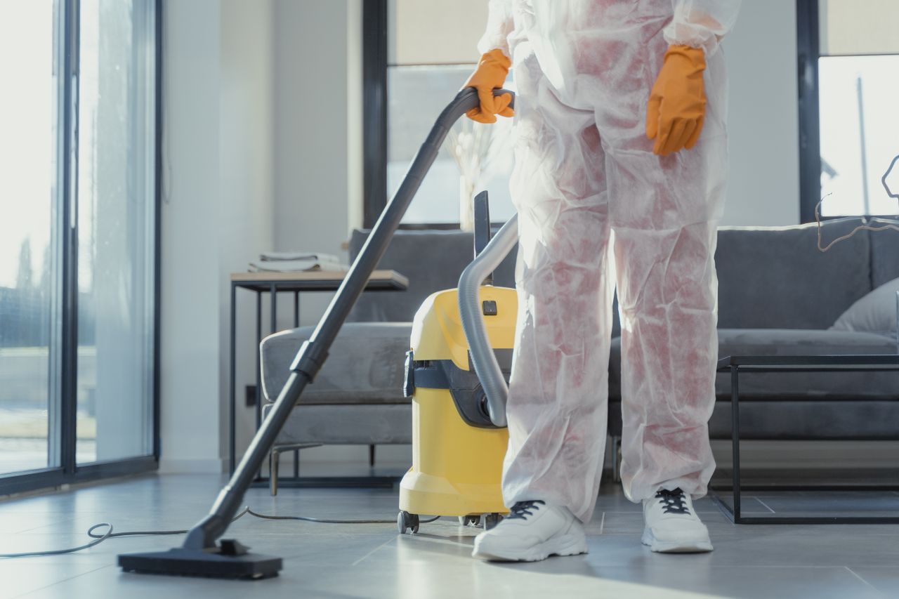 services-img A cleaner in protective coveralls and gloves vacuuming a modern living room.